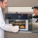 A man and woman using a Hatco Flav-R-Savor pass-through heated air curtain to put food into trays.