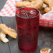 A red Cambro plastic tumbler filled with ice and a red drink on a table with a basket of pretzels.