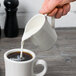 A white pitcher pouring milk into a cup of coffee.