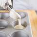 A person pouring dough into a Chicago Metallic jumbo muffin pan.