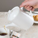 A person pouring coffee into a Tuxton Modena AlumaTux Pearl White coffee pot.