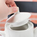 A hand holding a Tuxton Modena AlumaTux Pearl White China lid on a white teapot.