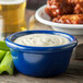 A Carlisle cobalt blue ramekin filled with white liquid on a table with celery sticks and wings.