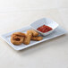 A Tuxton bright white square china bowl with fried fish sticks and a bowl of red sauce.