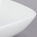A close-up of a Tuxton bright white square china bowl with a curved edge.