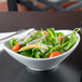 A Tuxton bright white china bowl filled with a salad with tomatoes, carrots, and spinach on a table.