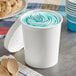 A stack of white paper cups with blue and white striped accents with a blue cup of ice cream and a wooden spoon.