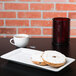 A Tuxton rectangular white china tray with a bagel and cream cheese next to a cup of coffee.