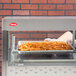 A person holding a tray of french fries in front of a Hatco countertop hot food display warmer.
