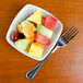 A TuxTrendz bright white square china bowl filled with sliced fruit with a fork.