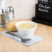 A Tuxton bright white china bouillon cup filled with chicken noodle soup on a napkin.