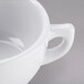 A close-up of a Tuxton TuxTrendz bright white cappuccino cup with a handle.
