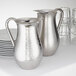 An American Metalcraft mirror finish stainless steel bell pitcher next to plates.