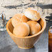 An American Metalcraft bamboo bowl filled with bread rolls on a table.