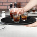 A hand holding a Carlisle non-skid serving tray with glasses of brown liquid.