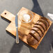 An American Metalcraft olive wood serving board with sliced bread and butter on it.