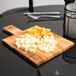 An American Metalcraft olive wood serving board with cubes of cheese on it.