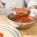 A hand using a Vollrath Jacob's Pride black round Spoodle to pour tomato sauce into a bowl.