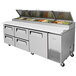 A Turbo Air pizza prep table with a stainless steel top and white drawers.