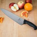 A Mercer Culinary Millennia chef knife next to an apple and an orange on a cutting board.