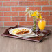 A mahogany plastic room service tray with breakfast food, a glass of orange juice, and a vase of yellow flowers.