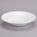 A close-up of a Tuxton San Marino AlumaTux Pearl White China bowl on a gray surface.