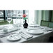 A table set with Tuxton AlumaTux Pearl White china plates and wine glasses.