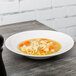A Tuxton San Marino AlumaTux Pearl White china bowl filled with soup and noodles.
