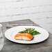 A Tuxton AlumaTux Pearl White China plate with salmon and green beans on a table.