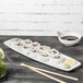 A rectangular Tuxton China plate with sushi on it and chopsticks on a table.