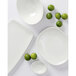 A group of Tuxton white china Capistrano bowls on a white surface.