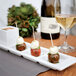 A rectangular white china plate with 4 compartments holding food on a table with a glass of white wine.