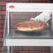 A gloved hand holds a pizza in a Hatco countertop display case.
