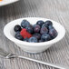 A Tuxton AlumaTux pearl white china fruit dish filled with blueberries and raspberries on a wooden table.