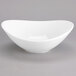 A Tuxton white china bowl with a curved edge on a white surface.