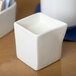 A close up of a square white Tuxton China creamer on a white surface.