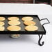 An American Metalcraft wrought iron griddle with pancakes cooking on a grill over a flame.