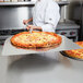 A chef using an American Metalcraft aluminum pizza peel to prepare a pizza.