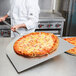 A chef using an American Metalcraft aluminum pizza peel to hold a pizza.