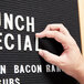 A person using an Aarco Helvetica letter to write "Lunch Special" on a black sign.
