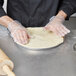 A person in plastic gloves using an American Metalcraft Super Perforated Pizza Pan to roll out pizza dough on a wood surface.