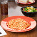 A bowl of salad and a plate of spaghetti on a colorful table with a brown GET Diamond Mardi Gras melamine bowl.