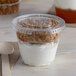 A Squat plastic parfait cup with yogurt, granola, and a spoon.