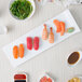 A white 10 Strawberry Street porcelain rectangular platter with sushi and other food on a table.
