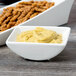 A white rectangular porcelain bowl filled with mustard next to a bowl of dip.
