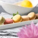 A row of colorful macaroons on a 10 Strawberry Street white rectangular porcelain dish.