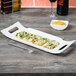 A white rectangular porcelain platter with food on a table.