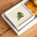 A rectangular white porcelain tray with 4 square white dishes, each with a white sauce and a fried potato.