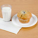 A muffin on a plate next to a Cambro Newport plastic tumbler filled with milk.
