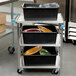 A Lakeside stainless steel utility cart with three shelves holding food containers.